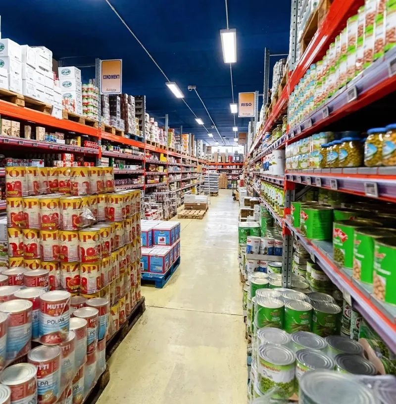 Corsia di magazzino con scaffali di conserve e pallet di pelati